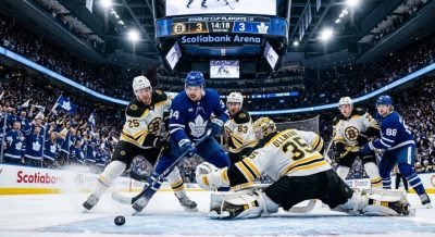 A tense NHL playoff moment showing players battling near the goal crease, crowd roaring in the background, scoreboard displaying overtime